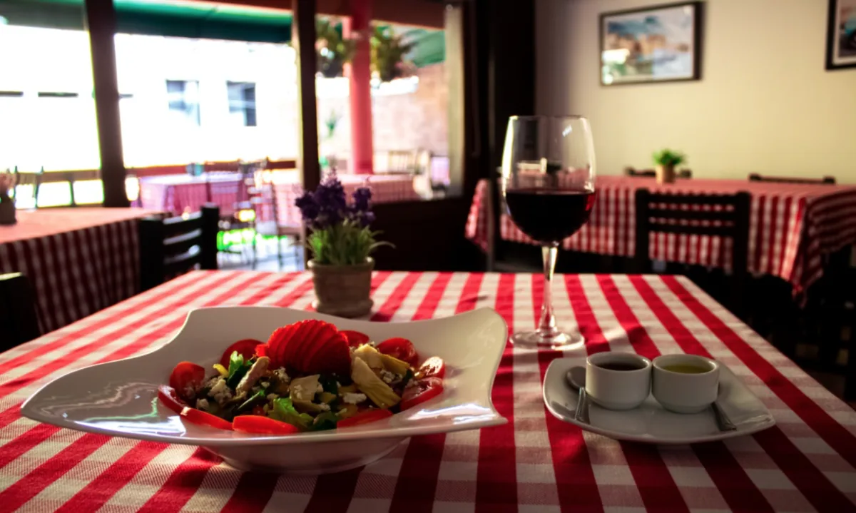 Mesa de Sapori con ensalada, una copa de vino y manteles a cuadros
